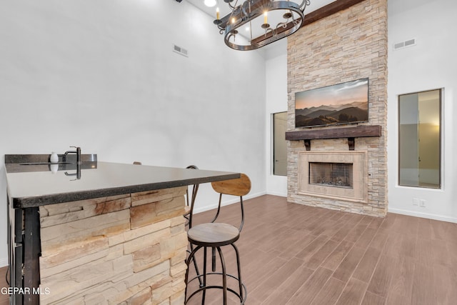 5833 Sundale Rd, El Paso, TX 79912 - kitchen featuring a stone fireplace, a towering ceiling, wood finished floors, a chandelier, and a breakfast bar
