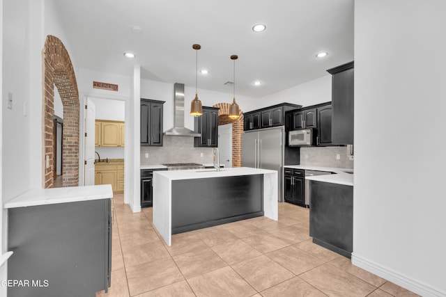 5833 Sundale Rd, El Paso, TX 79912 - kitchen featuring wall chimney exhaust hood, appliances with stainless steel finishes, light countertops, decorative backsplash, and an island with sink
