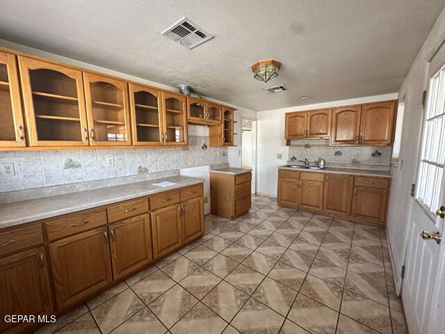 209 Durrill Rd, El Paso, TX 79915 - kitchen featuring brown cabinets, decorative backsplash, glass insert cabinets, a textured ceiling, and light countertops