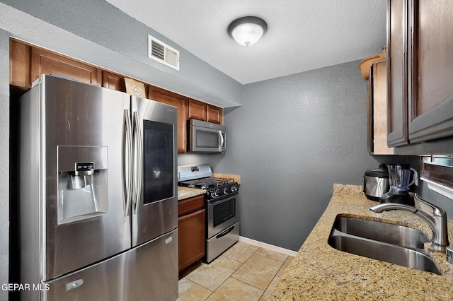 4640 Beacham St, El Paso, TX 79938 - kitchen featuring appliances with stainless steel finishes, light stone countertops, light tile patterned floors, brown cabinetry, and a textured ceiling