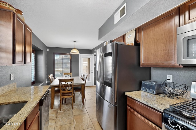 4640 Beacham St, El Paso, TX 79938 - kitchen with appliances with stainless steel finishes, light stone countertops, pendant lighting, a textured wall, and brown cabinetry