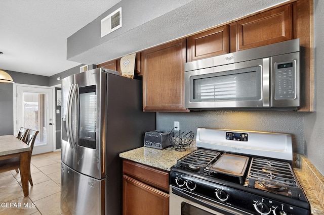 4640 Beacham St, El Paso, TX 79938 - kitchen with stainless steel appliances, light tile patterned floors, brown cabinets, and light stone counters