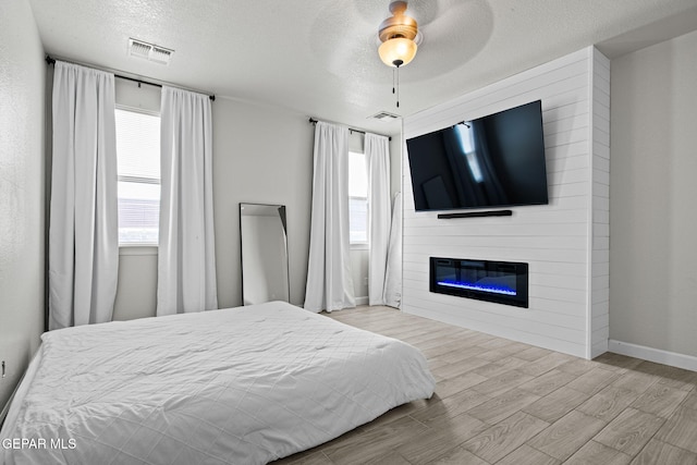 12334 Westbury, El Paso, TX 79928 - bedroom with wood finished floors, a textured ceiling, multiple windows, a glass covered fireplace, and a ceiling fan