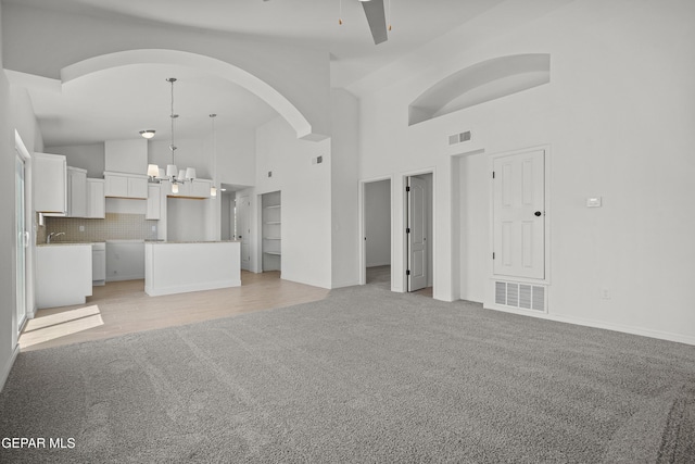 224 Penbridge Pl, El Paso, TX 79928 - unfurnished living room with light carpet, a chandelier, high vaulted ceiling, arched walkways, and ceiling fan