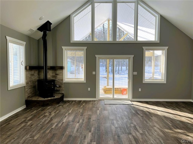 unfurnished living room with dark wood-type flooring, a wood stove, and high vaulted ceiling