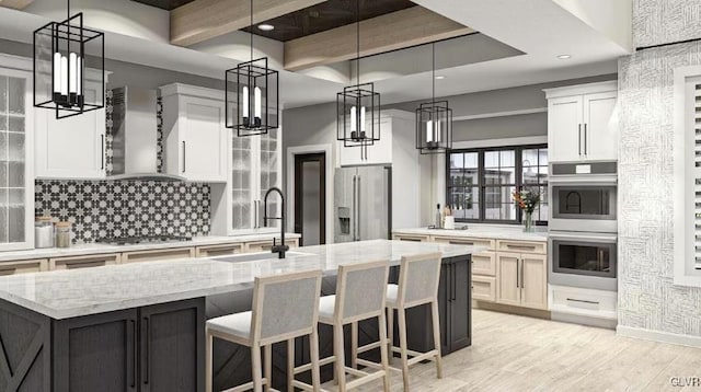 kitchen with wall chimney exhaust hood, light stone counters, a large island with sink, white cabinets, and appliances with stainless steel finishes