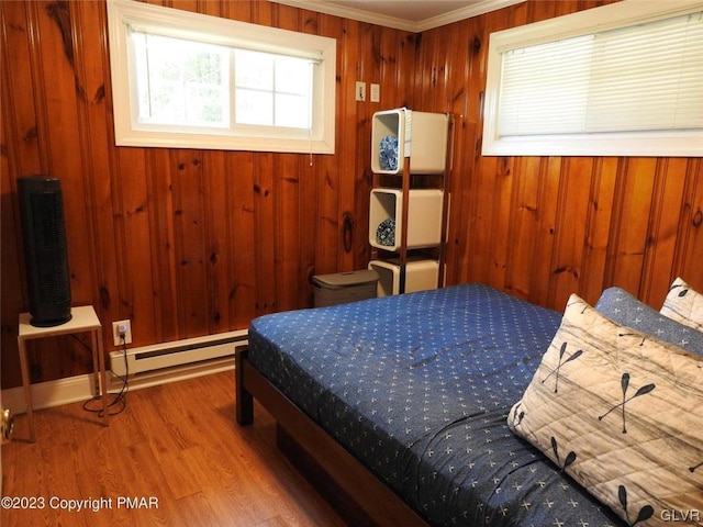 bedroom featuring ornamental molding, wood walls, baseboard heating, and hardwood / wood-style floors