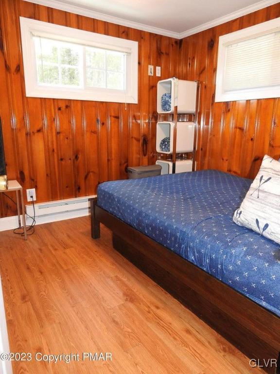 bedroom with crown molding, light hardwood / wood-style floors, wood walls, and a baseboard heating unit