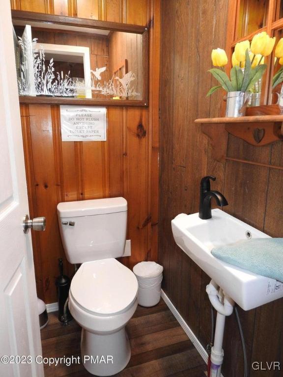 bathroom with toilet, wood walls, and hardwood / wood-style floors