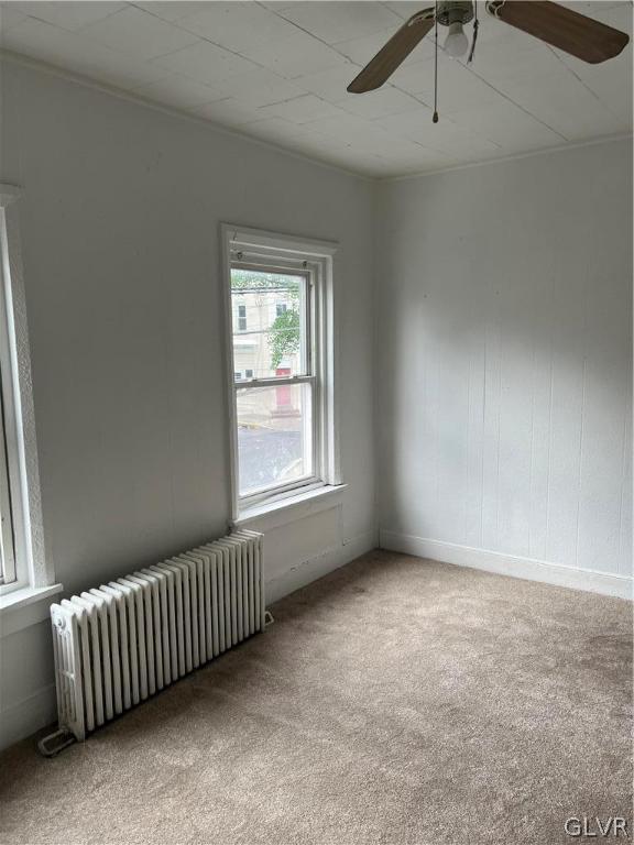 carpeted spare room with radiator heating unit and ceiling fan