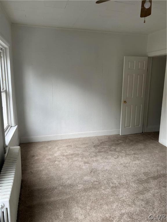 carpeted empty room with radiator and ceiling fan