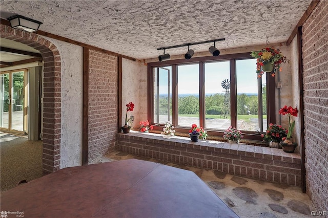 interior space featuring a textured ceiling, brick wall, and rail lighting