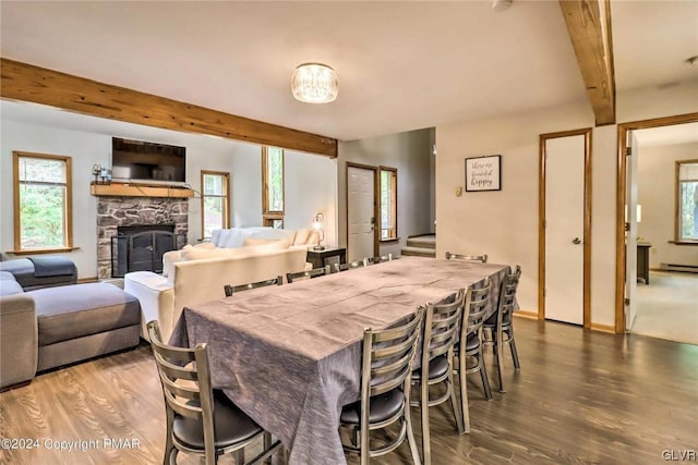 dining room with a healthy amount of sunlight, a stone fireplace, beam ceiling, and hardwood / wood-style flooring