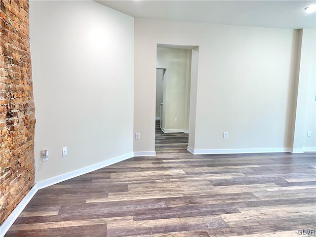 unfurnished room with brick wall and dark hardwood / wood-style flooring