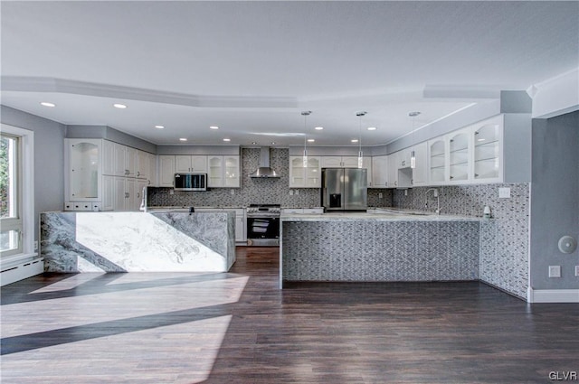 kitchen featuring dark hardwood / wood-style flooring, pendant lighting, appliances with stainless steel finishes, tasteful backsplash, and wall chimney exhaust hood