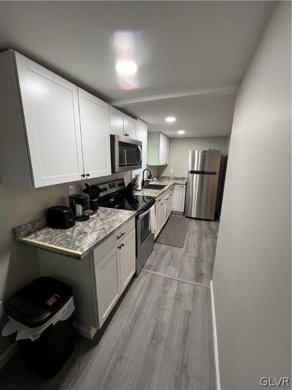 kitchen featuring appliances with stainless steel finishes, light hardwood / wood-style flooring, light stone counters, and white cabinetry