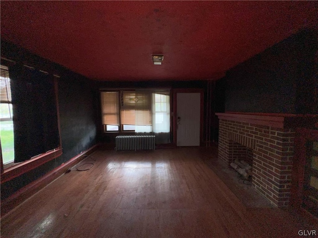 unfurnished living room featuring wood-type flooring, radiator, and a brick fireplace