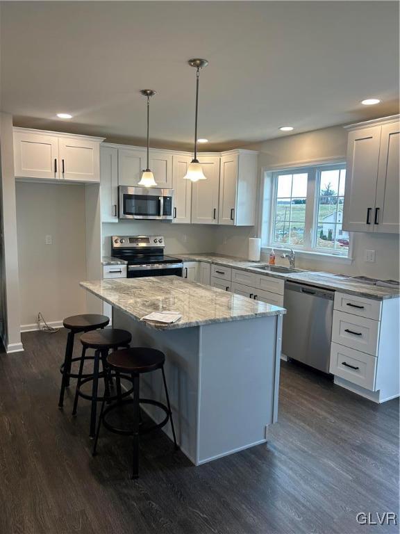 kitchen featuring white cabinets, hanging light fixtures, dark hardwood / wood-style floors, appliances with stainless steel finishes, and a kitchen island