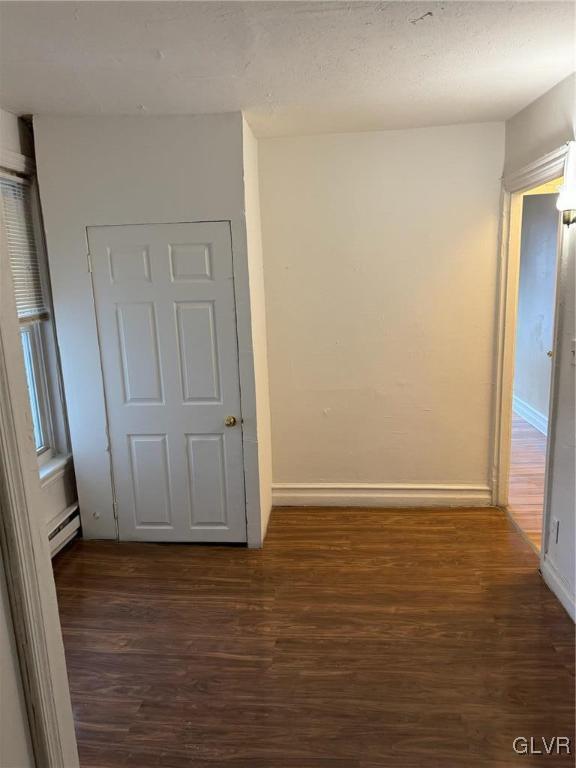 corridor featuring baseboard heating and dark hardwood / wood-style floors