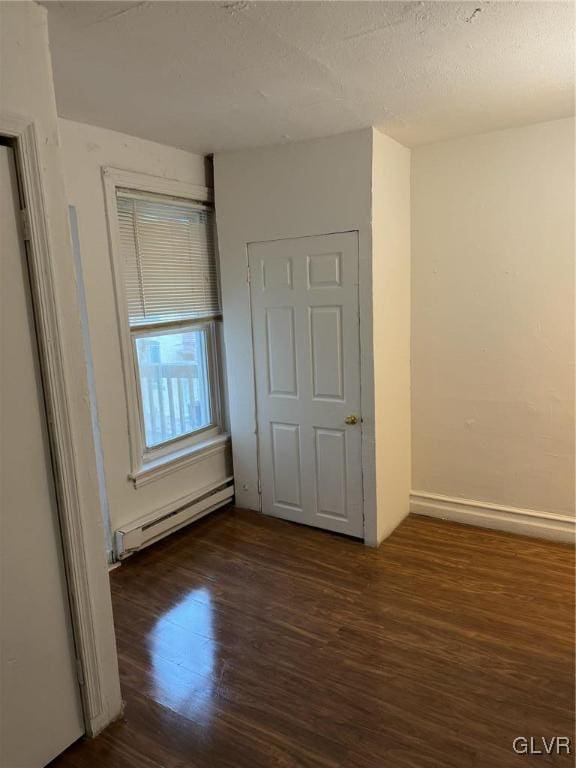 unfurnished bedroom with a textured ceiling, baseboard heating, and dark hardwood / wood-style flooring