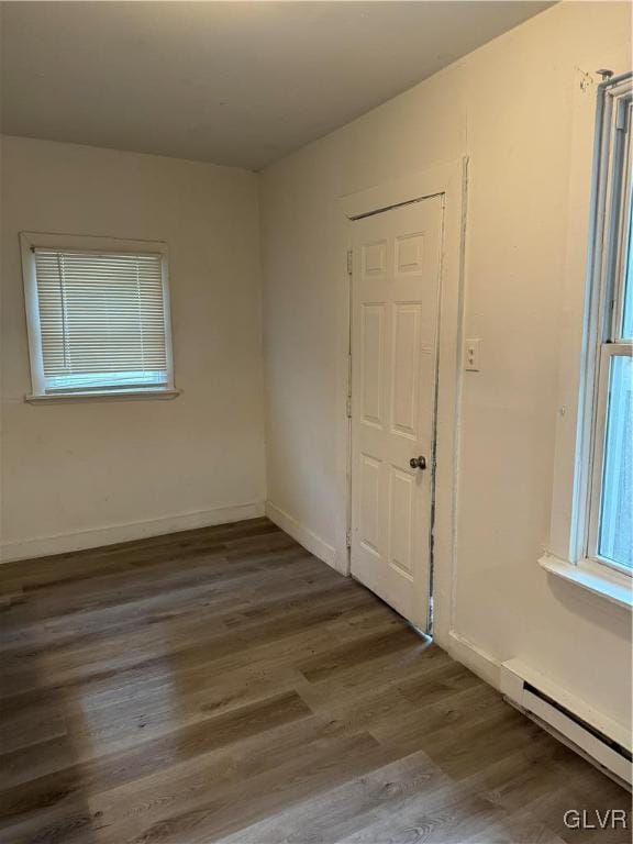 unfurnished room with baseboard heating and dark wood-type flooring