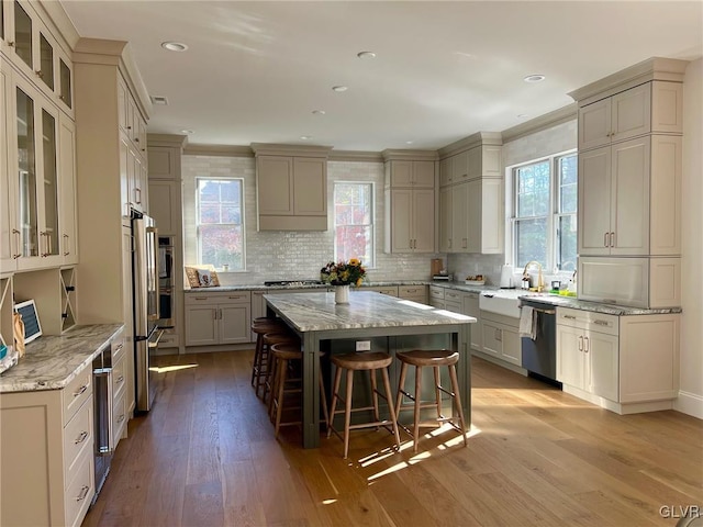 kitchen featuring a center island, appliances with stainless steel finishes, light hardwood / wood-style floors, light stone counters, and a breakfast bar area