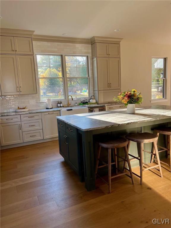 kitchen featuring light stone countertops, a center island, tasteful backsplash, light hardwood / wood-style flooring, and a breakfast bar