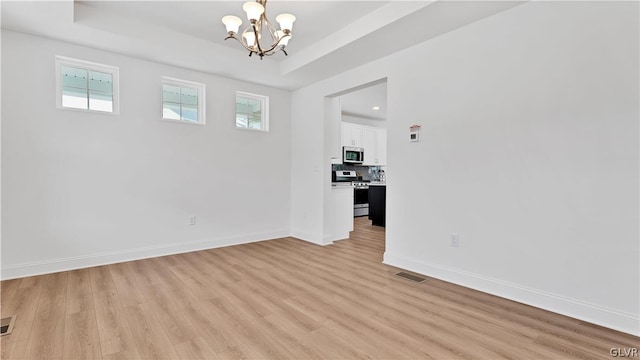 spare room featuring light hardwood / wood-style floors, a raised ceiling, and a chandelier