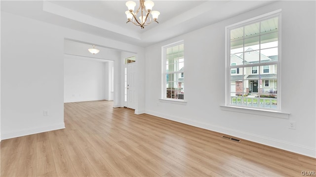 spare room featuring an inviting chandelier, light wood-type flooring, and a tray ceiling