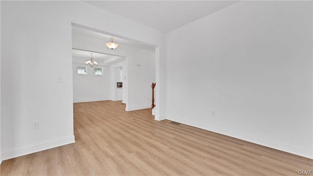 empty room with a chandelier and light wood-type flooring