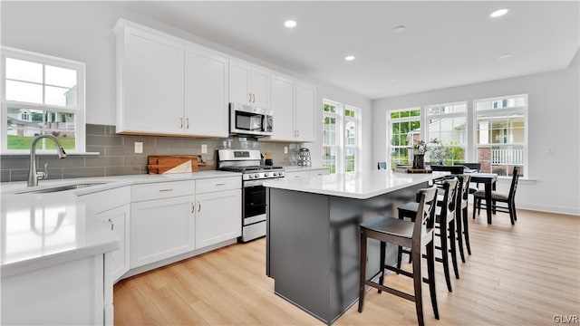 kitchen featuring white cabinets, gas stove, backsplash, light hardwood / wood-style floors, and a center island