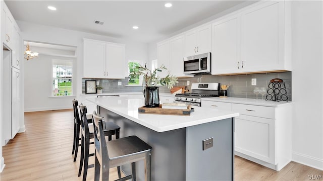 kitchen featuring white cabinetry, light hardwood / wood-style flooring, a center island, appliances with stainless steel finishes, and decorative backsplash