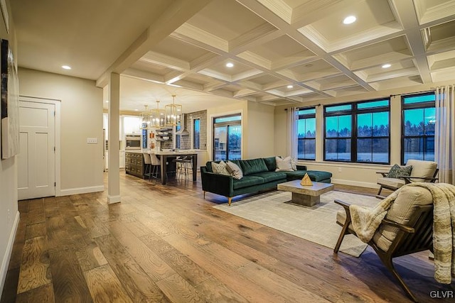 living room featuring coffered ceiling, beamed ceiling, a notable chandelier, hardwood / wood-style flooring, and a healthy amount of sunlight