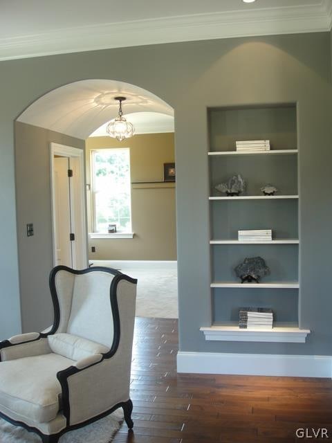 interior space featuring ornamental molding, hardwood / wood-style floors, built in shelves, and a notable chandelier