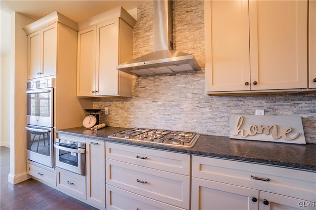 kitchen with dark stone countertops, stainless steel appliances, decorative backsplash, dark hardwood / wood-style floors, and wall chimney range hood