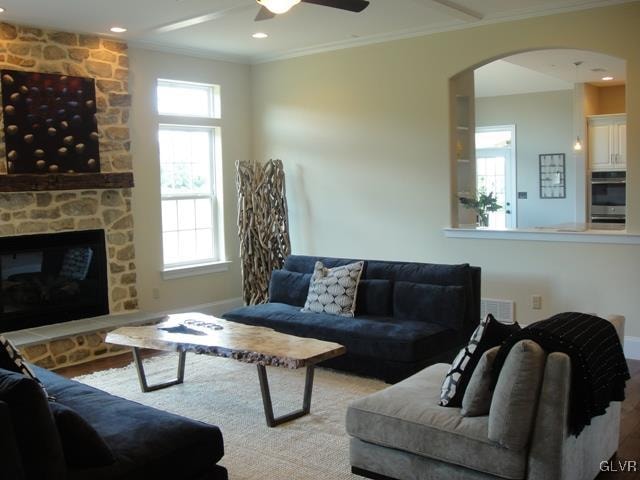 living room with ornamental molding, a wealth of natural light, ceiling fan, and a stone fireplace