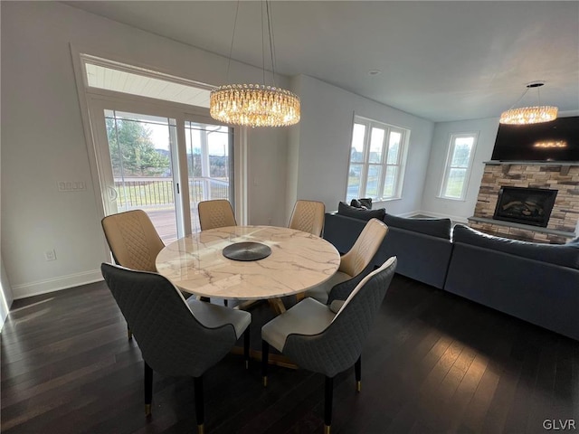 dining room with a notable chandelier, a stone fireplace, dark hardwood / wood-style flooring, and plenty of natural light