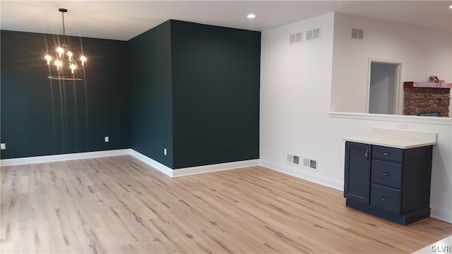 unfurnished room featuring a notable chandelier, light wood-type flooring, and a stone fireplace