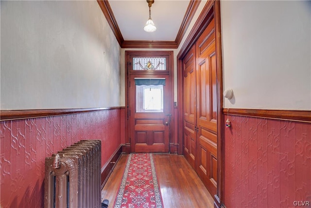 doorway to outside with radiator heating unit, hardwood / wood-style floors, and crown molding