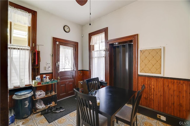 dining room with a ceiling fan, wainscoting, and wooden walls