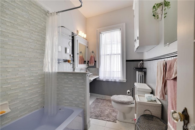 full bath featuring toilet, a wainscoted wall, shower / bathtub combination with curtain, and tile patterned floors