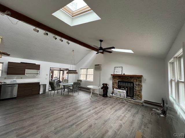 living room with ceiling fan, wood-type flooring, a stone fireplace, and vaulted ceiling with skylight