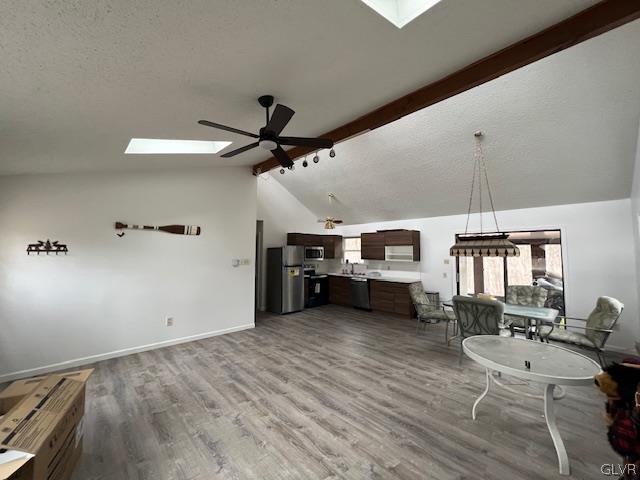 unfurnished living room with ceiling fan, wood-type flooring, a skylight, and beam ceiling