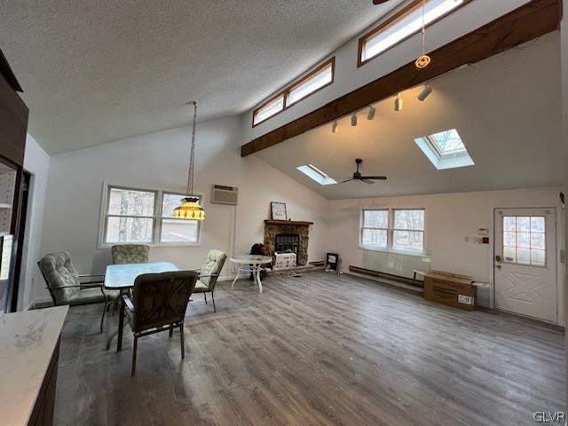 dining area with ceiling fan, a stone fireplace, a skylight, beamed ceiling, and wood-type flooring