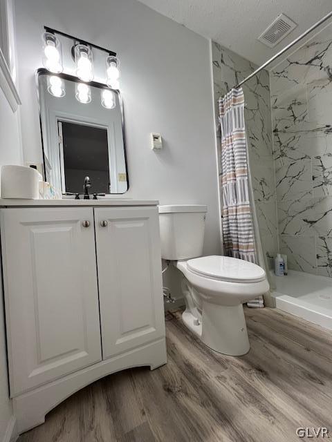 bathroom with hardwood / wood-style floors, walk in shower, vanity, and toilet