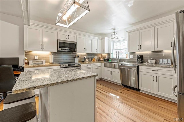 kitchen with a breakfast bar area, light hardwood / wood-style flooring, stainless steel appliances, and white cabinetry