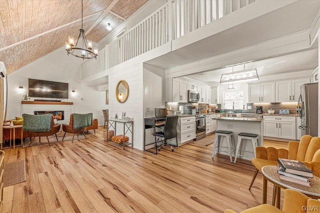 living room with light hardwood / wood-style flooring, a chandelier, a brick fireplace, a towering ceiling, and sink