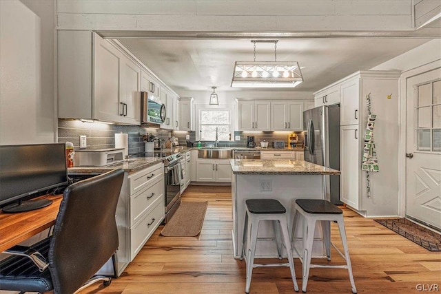 kitchen with white cabinetry, stainless steel appliances, light wood-type flooring, dark stone countertops, and a kitchen island