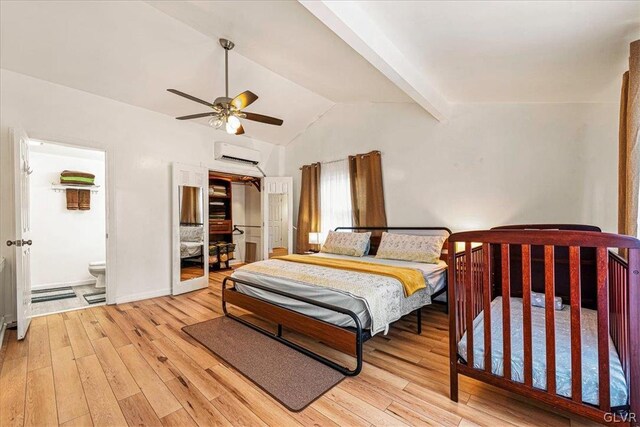 bedroom featuring a wall mounted air conditioner, ceiling fan, light hardwood / wood-style floors, ensuite bathroom, and lofted ceiling with beams