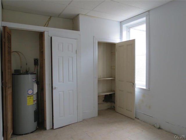 unfurnished bedroom featuring electric water heater, a paneled ceiling, and light tile patterned floors